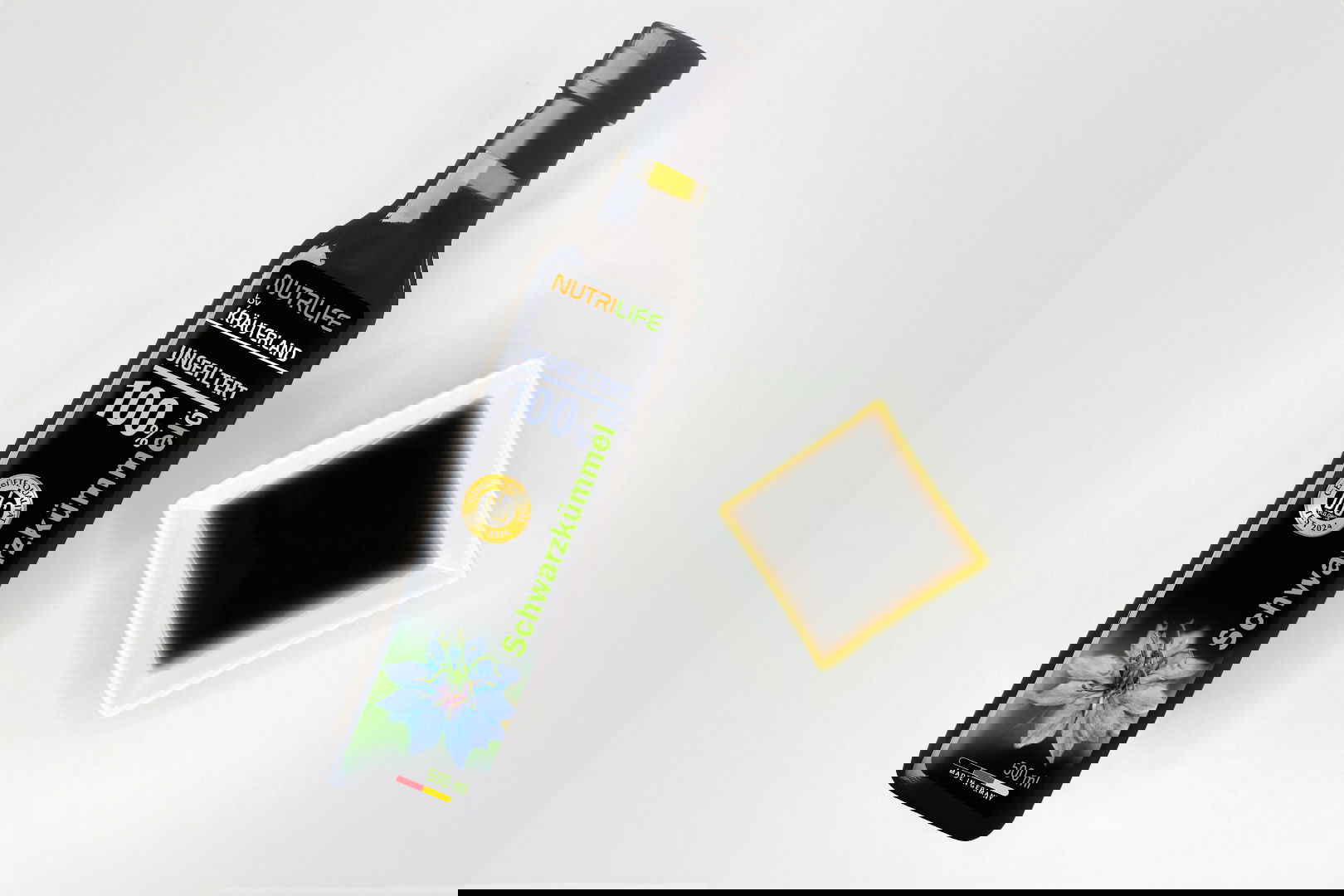 Nutrilife by Kräuterland Schwarzkümmelöl 500 ml kaltgepresst und ungefiltert in Glasflasche neben Schälchen mit dem gleichen dunklen Öl zur Veranschaulichung der natürlichen Farbe