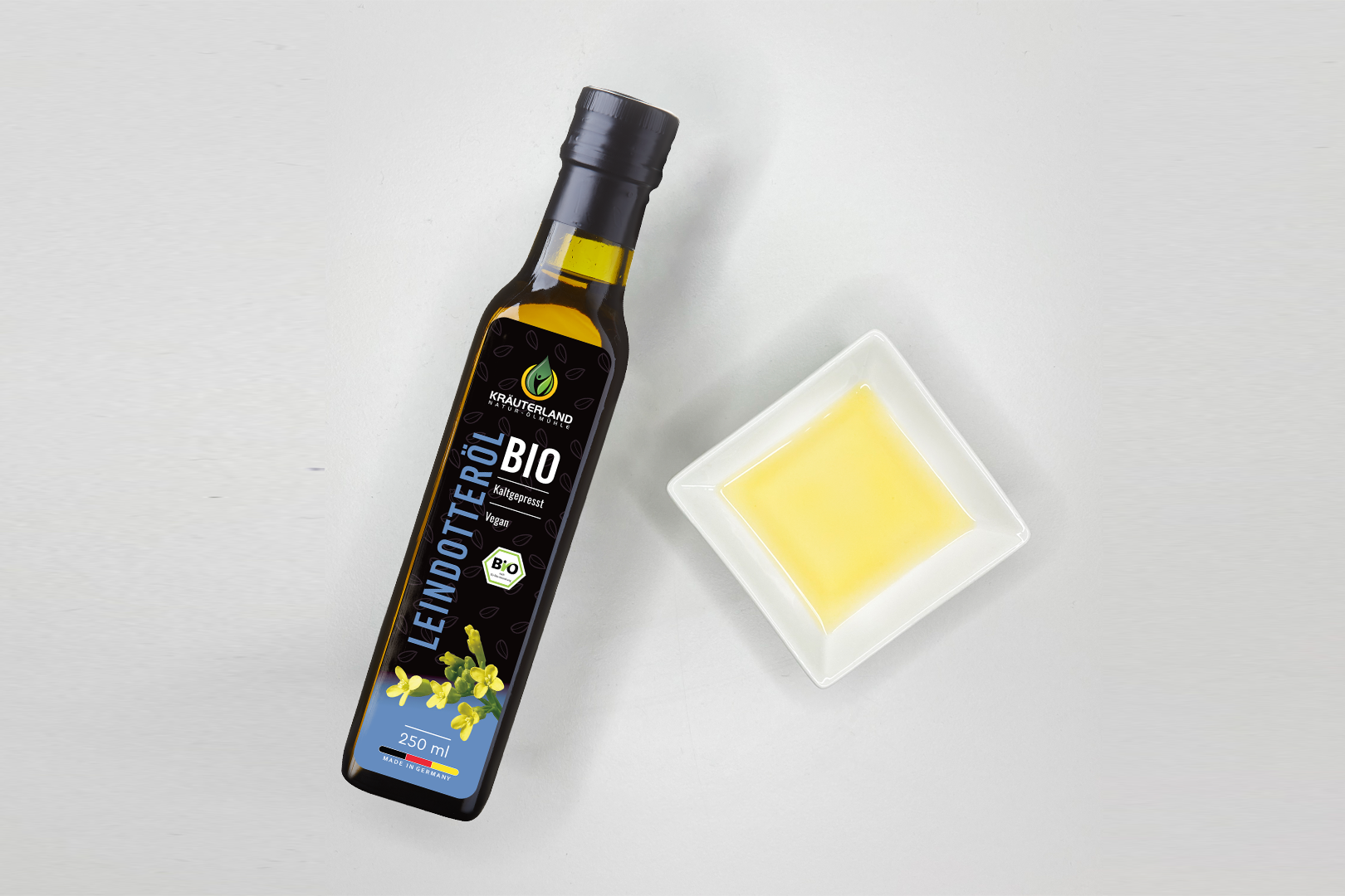 Kräuterland Bio Leindotteröl 250 ml kaltgepresst in Glasflasche neben Schälchen mit hellgelbem Öl zur Darstellung der Farbe und Konsistenz