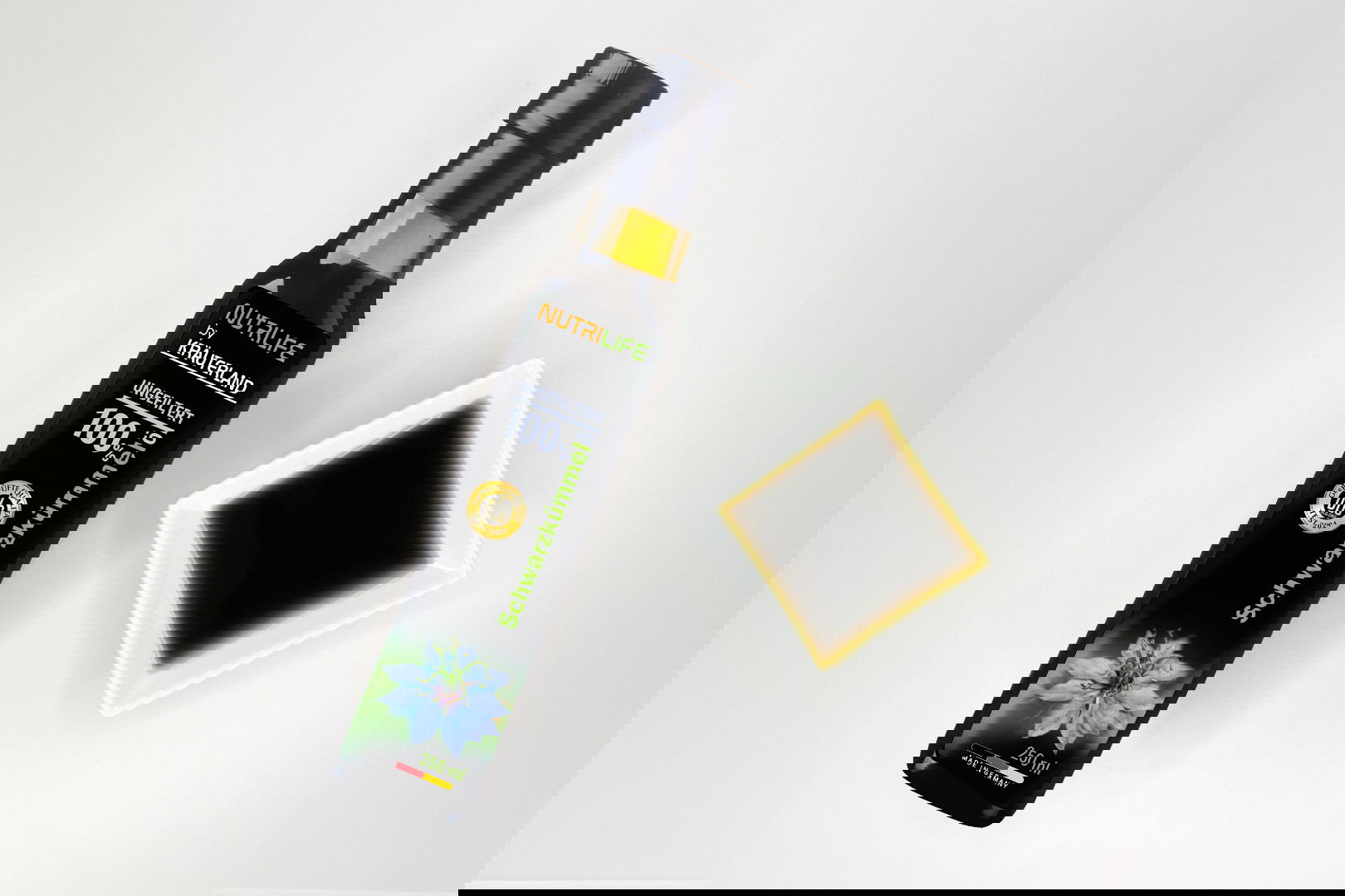 Nutrilife by Kräuterland Schwarzkümmelöl 250 ml ungefiltert in Glasflasche neben Schälchen mit dem gleichen dunklen Öl zur Veranschaulichung der natürlichen Farbe