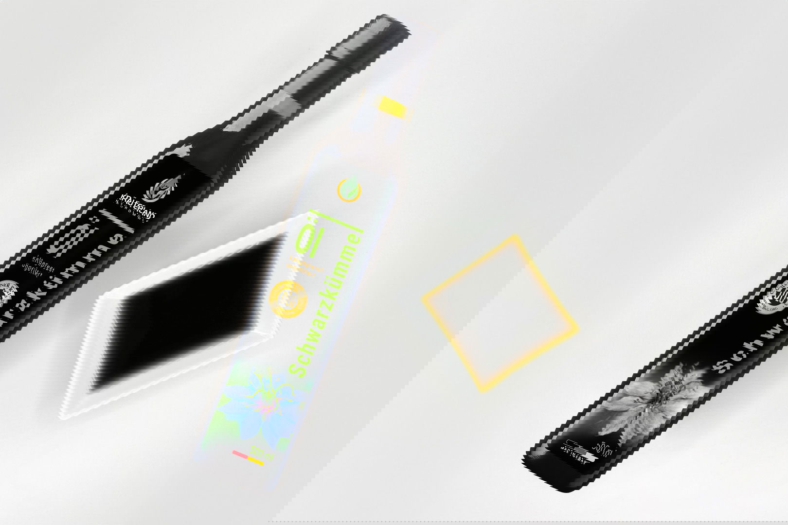 Kräuterland Schwarzkümmelöl 500 ml kaltgepresst und ungefiltert in Glasflasche neben Schälchen mit dem gleichen dunklen Öl zur Veranschaulichung der natürlichen Farbe