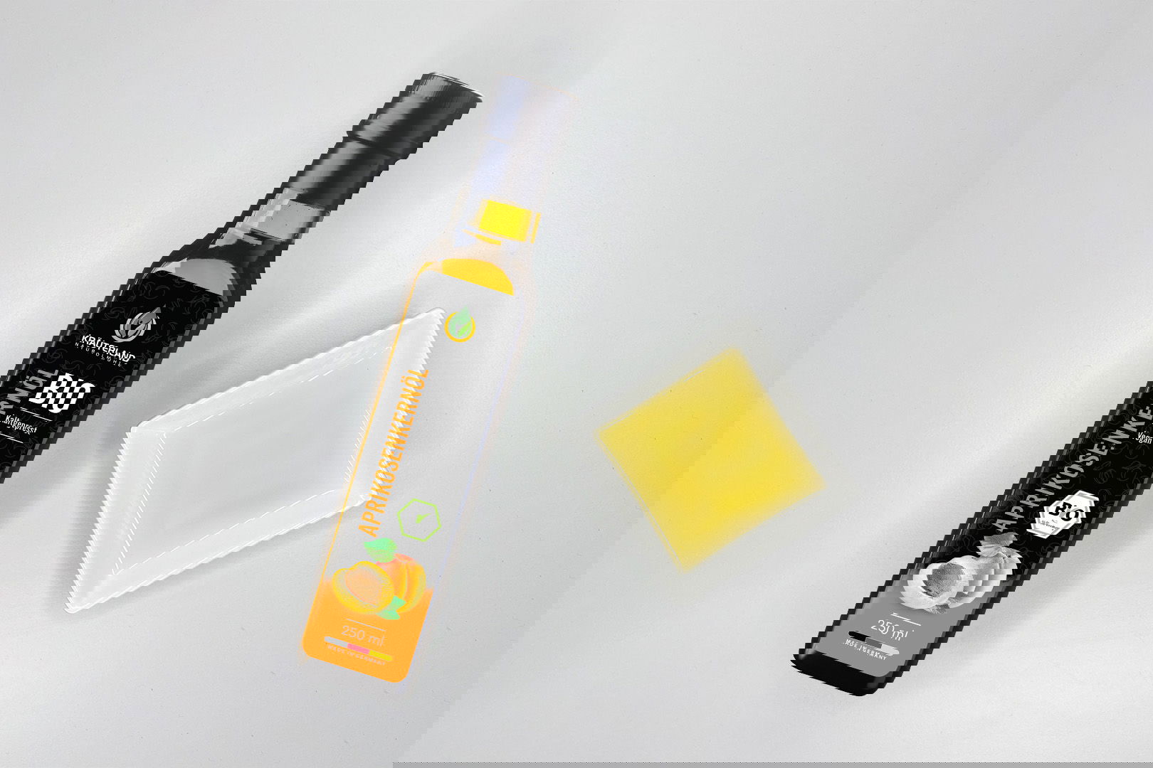 Kräuterland Bio Aprikosenkernöl kaltgepresst in Glasflasche neben Schälchen mit dem gleichen Öl zur Veranschaulichung