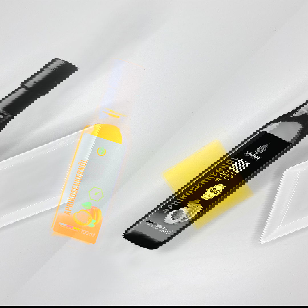 Kräuterland Bio Aprikosenkernöl 100 ml kaltgepresst neben Schälchen mit hellgelbem Öl zur Farbdarstellung