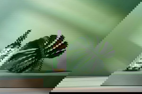 Vitamin K2 Tropfenflasche von Kräuterland auf grünem Podest mit großem Monstera Blatt im Hintergrund