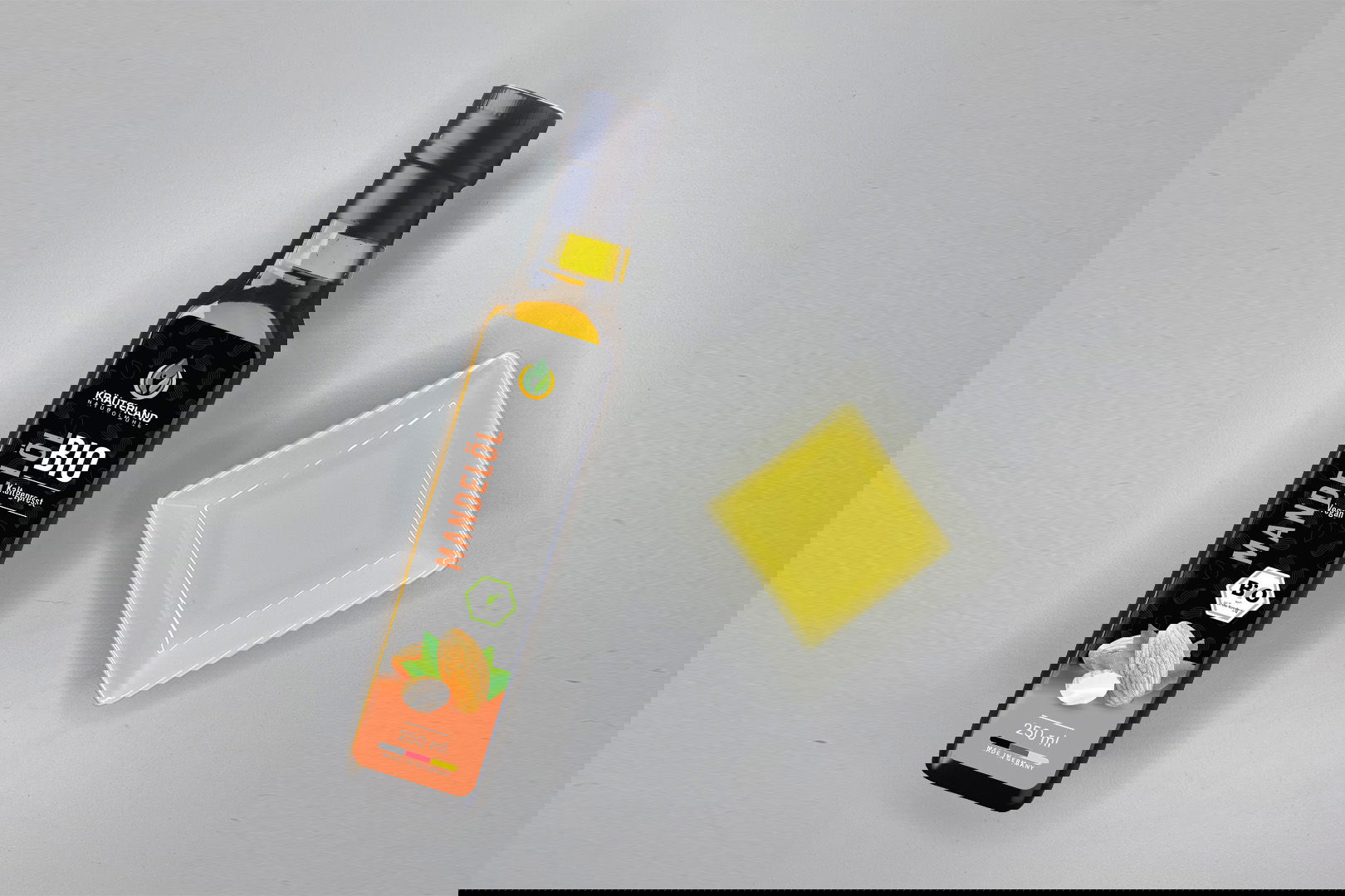 Kräuterland Bio Mandelöl 250 ml kaltgepresst in Glasflasche neben Schälchen mit dem gleichen hellgelben Öl zur Veranschaulichung der Farbe