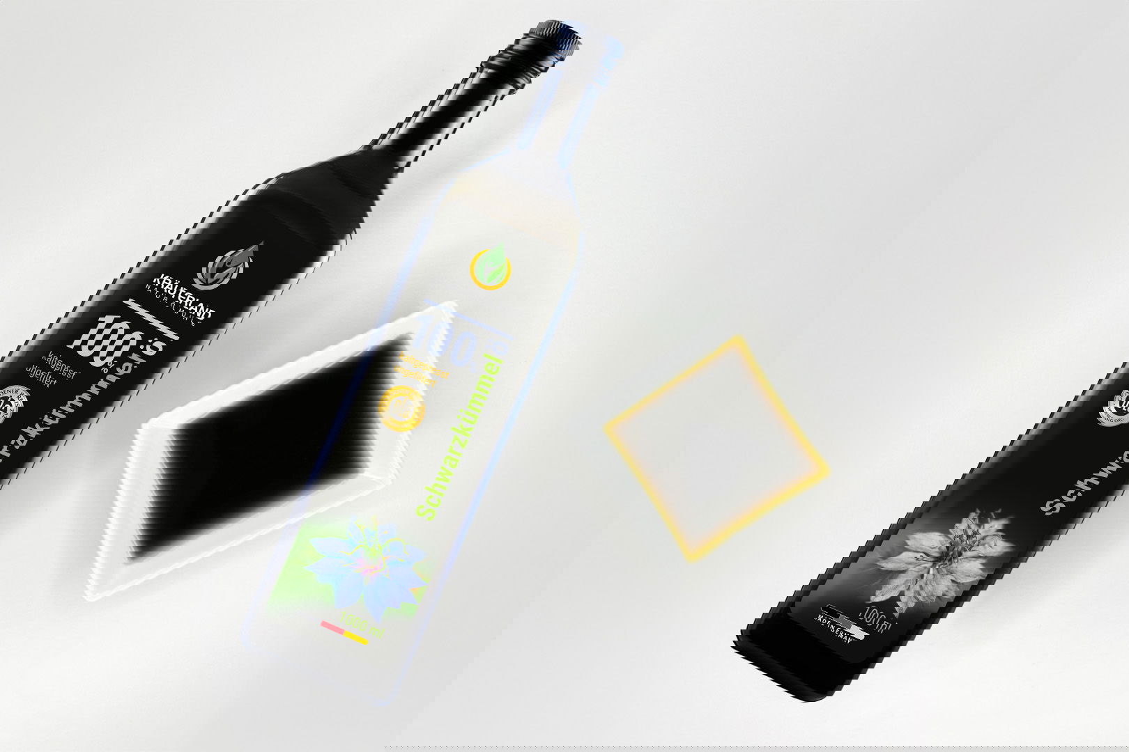 Kräuterland Schwarzkümmelöl 1000 ml kaltgepresst und ungefiltert in Glasflasche neben Schälchen mit dem gleichen dunklen Öl zur Veranschaulichung der natürlichen Farbe