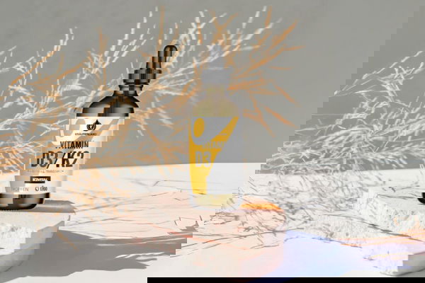 Vitamin D3 K2 Tropfenflasche von Kräuterland auf hellem Podest mit getrockneten Pflanzen im Hintergrund