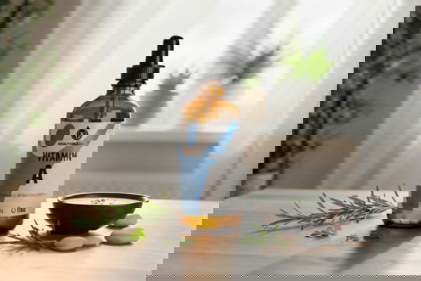 Vitamin A Tropfenflasche von Kräuterland auf Holztisch mit Kräutern im Vordergrund