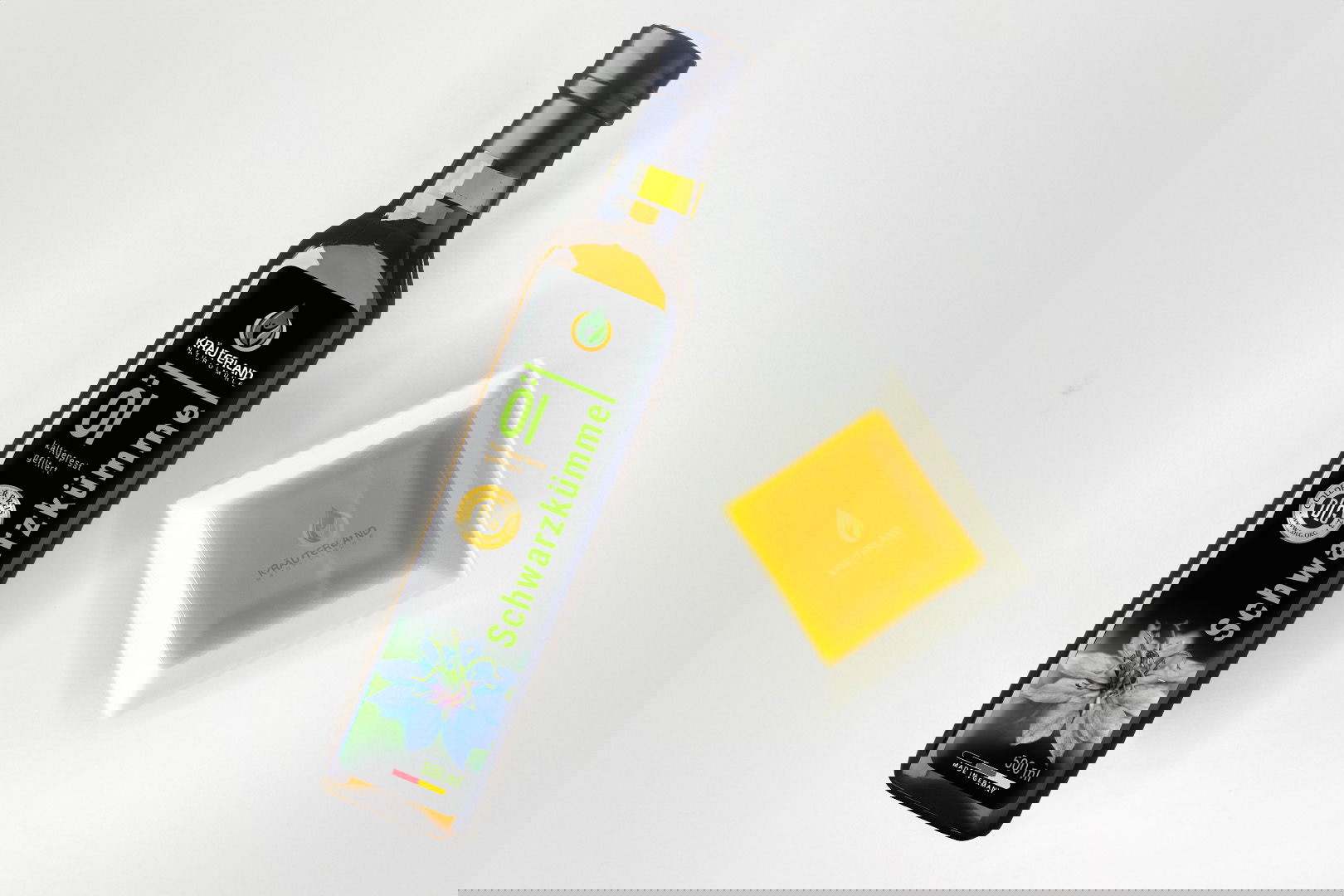 Kräuterland Schwarzkümmelöl kaltgepresst gefiltert in Glasflasche neben Schälchen mit dem gleichen goldgelben Öl zur Veranschaulichung der Farbe