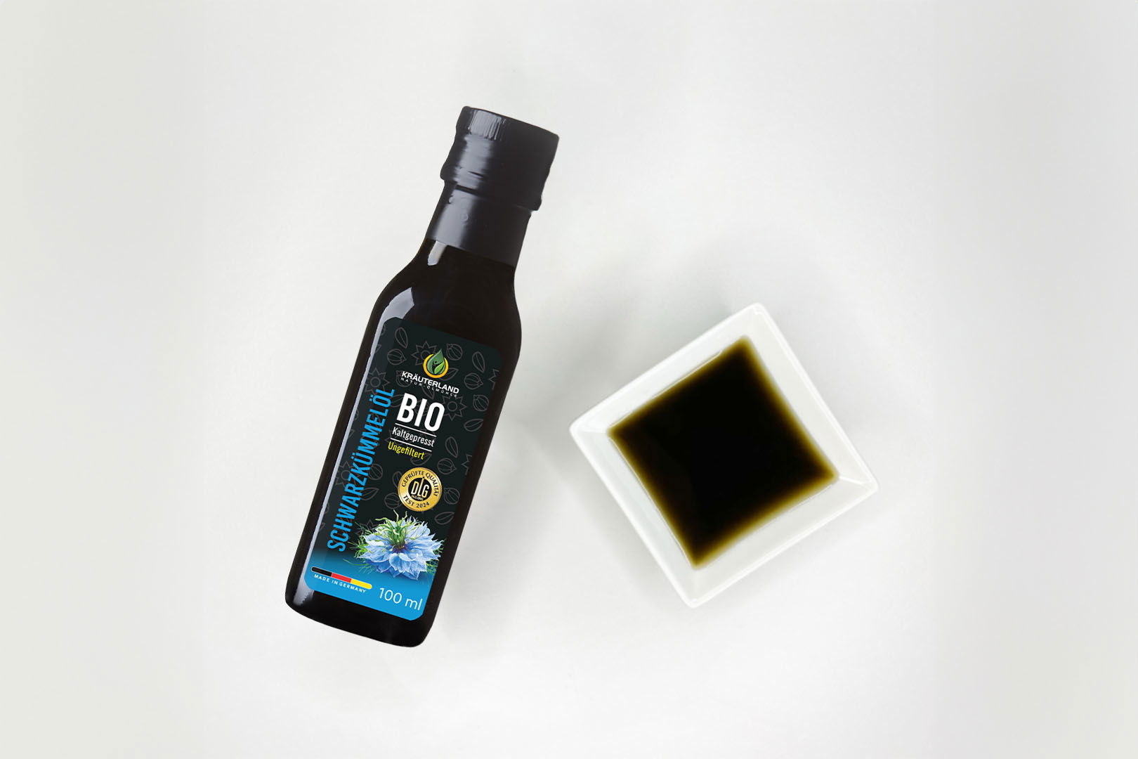 Kräuterland Bio Schwarzkümmelöl 100 ml kaltgepresst und ungefiltert in Glasflasche neben Schälchen mit dem gleichen dunklen Öl zur Veranschaulichung der natürlichen Farbe