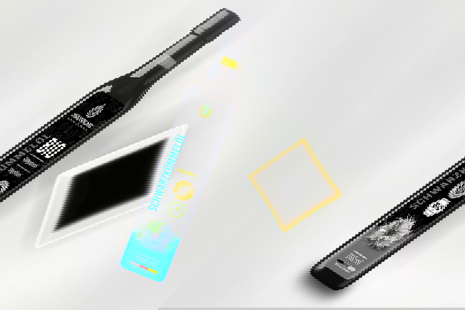 Kräuterland Bio Schwarzkümmelöl 500 ml kaltgepresst und ungefiltert in Glasflasche neben Schälchen mit dem gleichen dunklen Öl zur Veranschaulichung der natürlichen Farbe