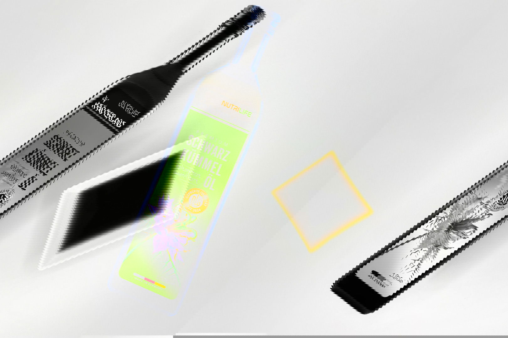 Nutrilife by Kräuterland Premium Schwarzkümmelöl 1000 ml kaltgepresst und ungefiltert in Glasflasche neben Schälchen mit dem gleichen dunklen Öl zur Veranschaulichung der natürlichen Farbe