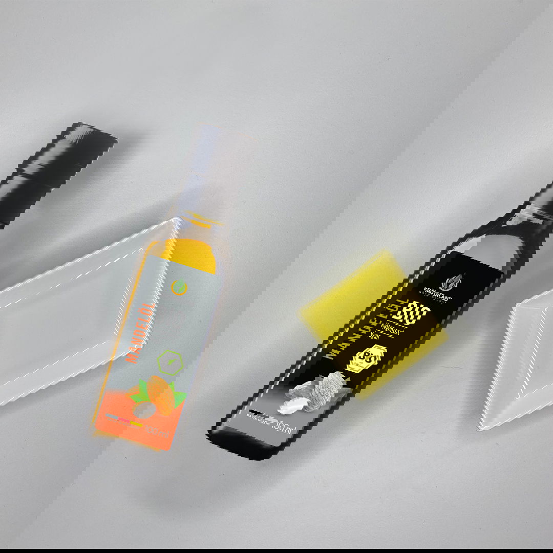 Bio Mandelöl von Kräuterland neben einer Glasschale mit hellgelbem Öl auf hellem Untergrund