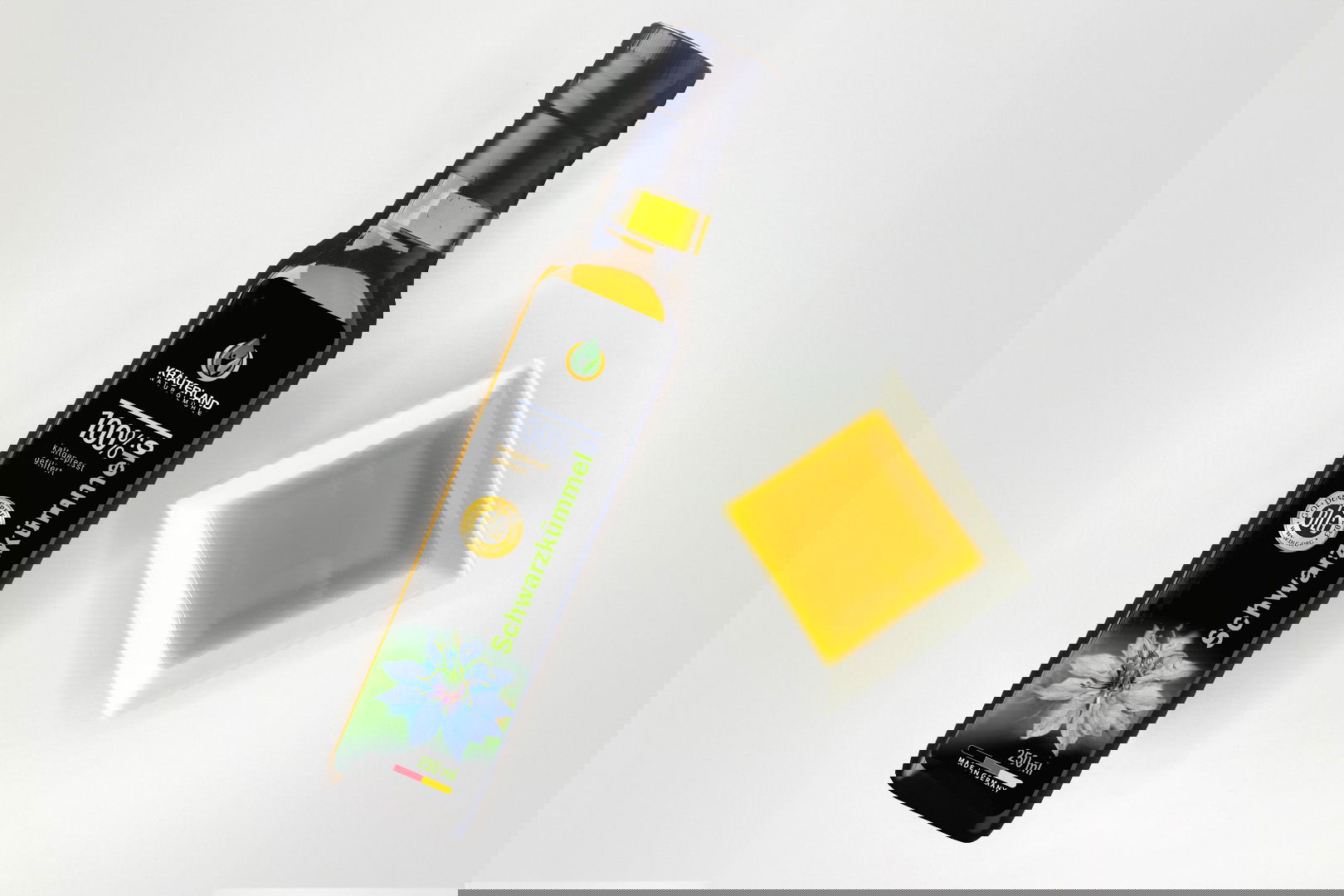 Kräuterland Schwarzkümmelöl 250 ml kaltgepresst und gefiltert in Glasflasche neben Schälchen mit dem gleichen goldgelben Öl zur Veranschaulichung der Farbe