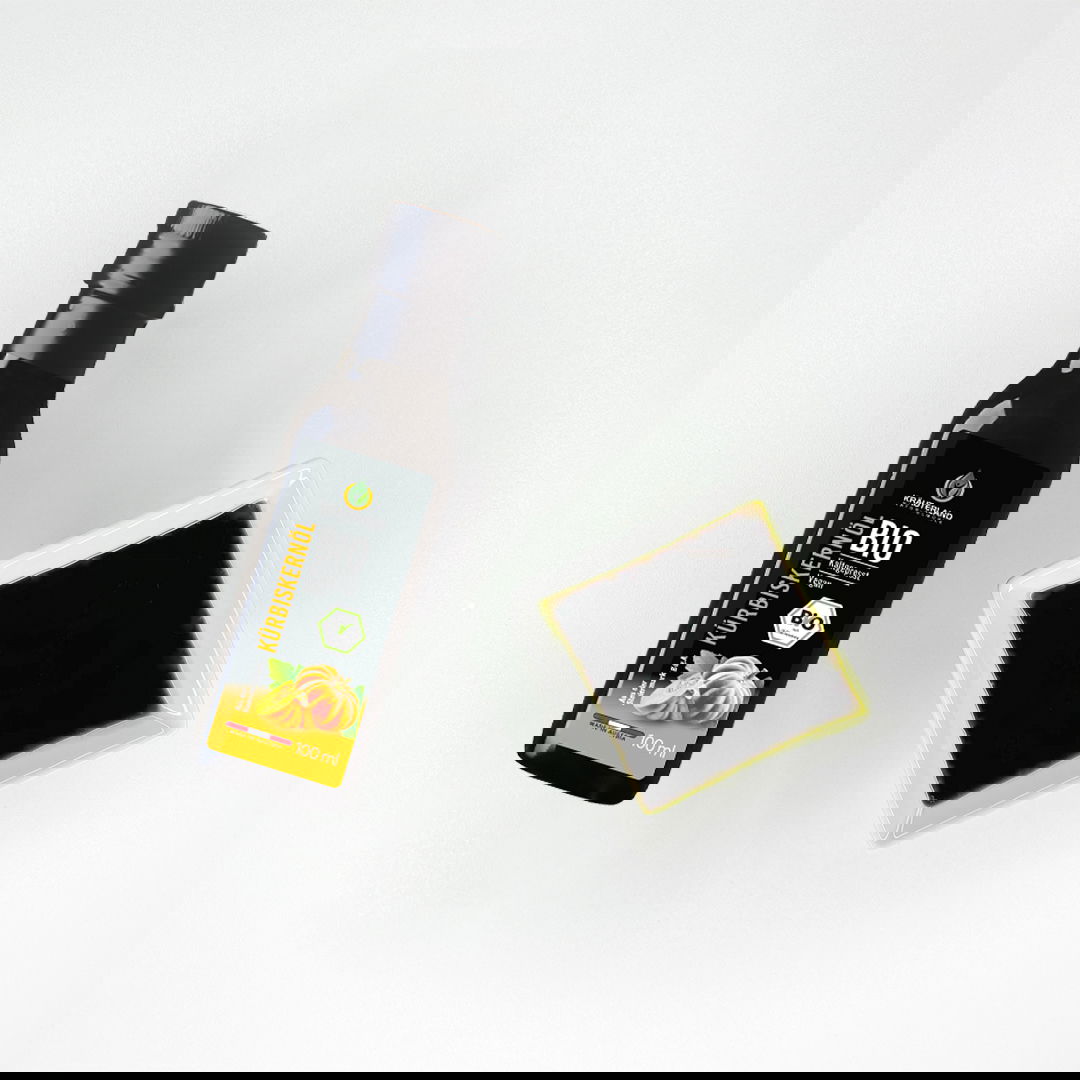 Bio Kürbiskernöl von Kräuterland neben einer Schale mit tiefgrünem Öl auf hellem Hintergrund